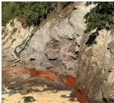 Heaps of sand, soil and stones at the base of a cliff, and a red sediment layer caused by iron oxide