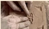 Hands building a clay face on a slab by adding moist clay for the forehead, eyebrows, eyes, nose, mouth and chin