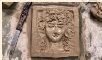A finished clay relief of a face resting on a flat surface to dry slowly over several days before painting