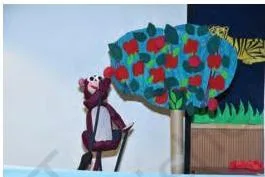 A tree prop with a monkey puppet reaching to pluck an apple, the monkey's hand moved by a stick
