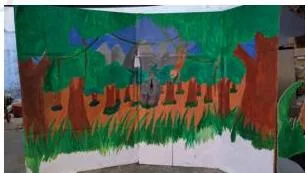 A painted backdrop showing a jungle with animals, the setting for a puppet show scene