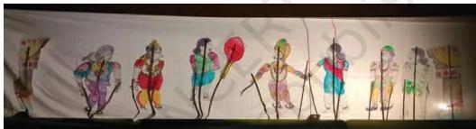 A shadow puppet show where light and the dark shadow of a puppet on a screen tell a story from the ancient epics